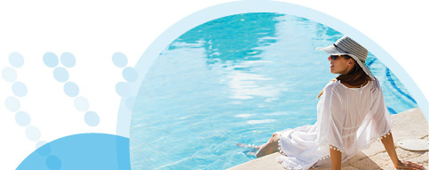 אישה עם כובע ובגדים לבנים יושבת על שפת הבריכה